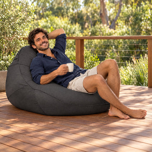 Big Boppa charcoal outdoor bean bag chair on a timber deck with a man relaxing holding a mug