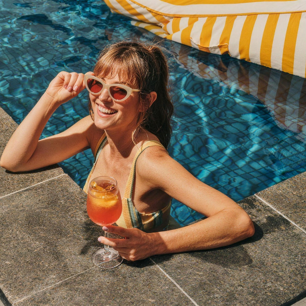 Guest with a spritz at the edge of the rooftop pool at Le Méridien Melbourne, with a yellow stripe Costa Pool bean bag floating behind