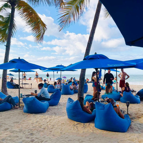 Guests on blue bean bags under blue umbrellas and palm trees on Ocean Park Beach at Numero Uno Beach House, San Juan, Puerto Rico