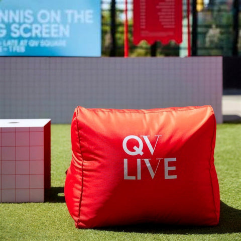 Red QV LIVE branded bean bag on the lawn in QV Square, Melbourne, in front of the Tennis on the Big Screen sign