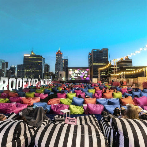 Striped Costa loungers and colourful Media Lounge bean bags facing the screen at Rooftop Movies, with the Perth skyline at dusk