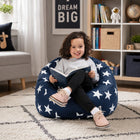 smiling young girl sitting on a blue bean bag chair with white stars reading a book — thumbnail 5