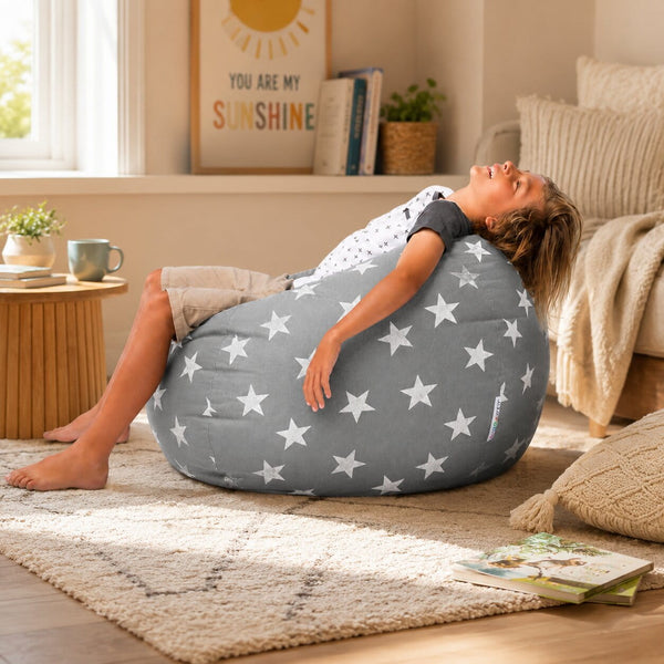 smiling young boy laying back on a grey bean bag chair with silver stars — image 4
