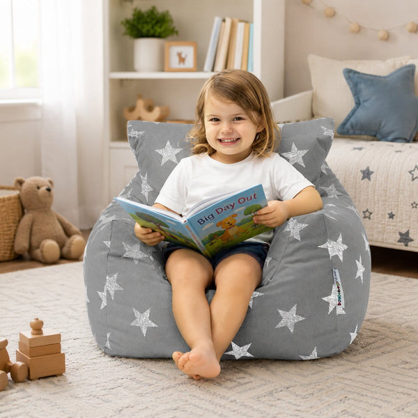 smiling young girl sitting on a grey bean bag chair with silver stars reading a book — image 5