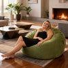 Woman sitting on a green bean bag in a cozy living room with a fireplace.