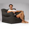Man sitting on a large black bean bag chair against a gray background
