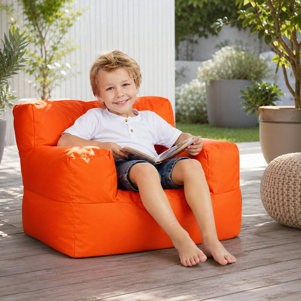 smiling young boy posing on an orange kids bean bag chair outdoors — image 7