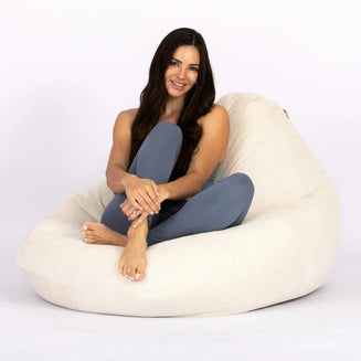 Woman sitting on a large beige bean bag chair against a white background