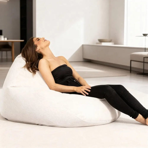 Woman relaxing on a white corduroy bean bag chair in a modern living room.