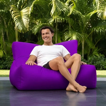 Person sitting on a purple bean bag chair outdoors with greenery in the background