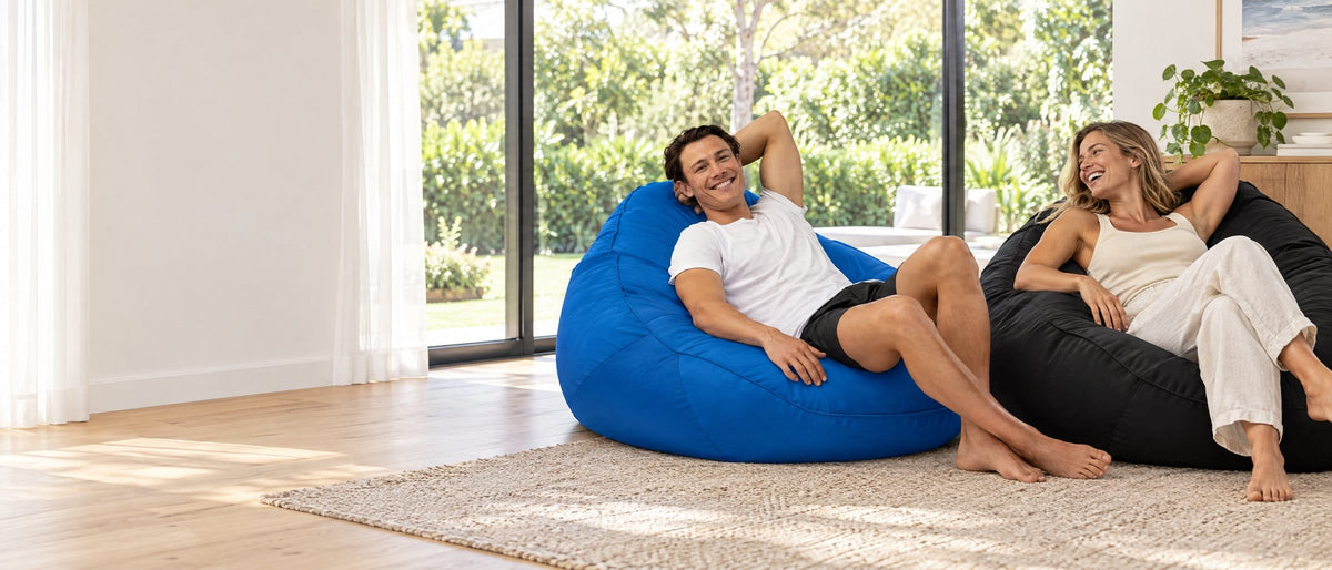 Two friends relaxing on blue and black Big Boppa bean bag chairs in a bright living room