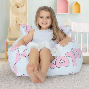 Child sitting on a bean bag with pink and white design in a room with toys and colorful boxes.