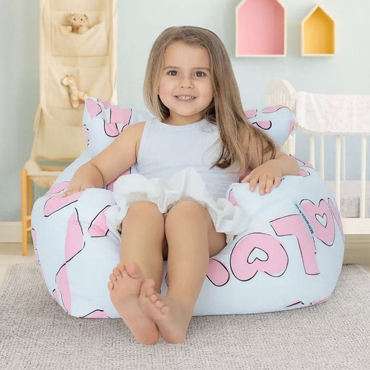 Child sitting on a bean bag with pink and white design in a room with toys and colorful boxes.