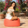 Woman sitting on a bean bag chair in a garden setting with flowers and plants around.