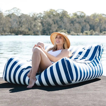 Woman sitting on a blue and white striped bean bag by a lake