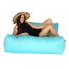 Woman sitting on a light blue bean bag lounger wearing a black dress and straw hat.
