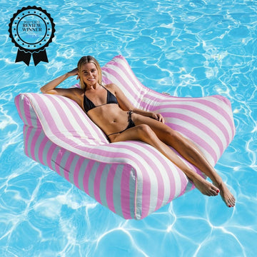 Woman lounging on a pink striped bean bag pool float in clear blue water with a 'Product Review Winner' badge.