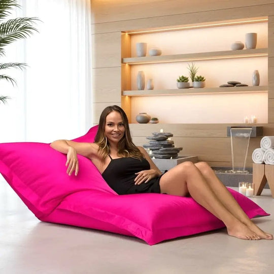 Woman sitting on a pink bean bag chair in a spa-like setting with shelves and plants.
