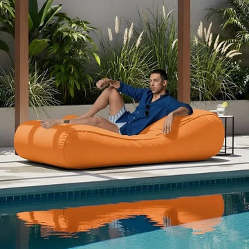 Man relaxing on an orange bean bag by a pool with plants in the background