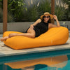 Woman relaxing on a large orange bean bag sun lounge by a pool with plants in the background