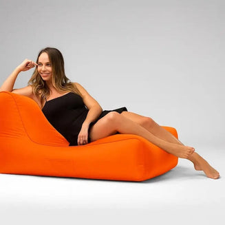 Woman in a black dress sitting on an orange bean bag chair against a gray background