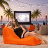 Woman lounging on an orange bean bag chair in a beachside movie theater setting.