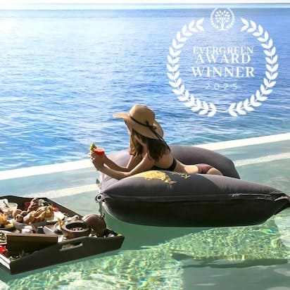 Woman relaxing on a floating device in a pool with a scenic view, holding a drink.