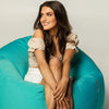Woman sitting on a teal bean bag chair against a plain background
