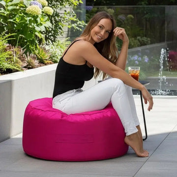 Woman sitting on a pink bean bag chair outdoors with plants and a glass of iced tea in the background.
